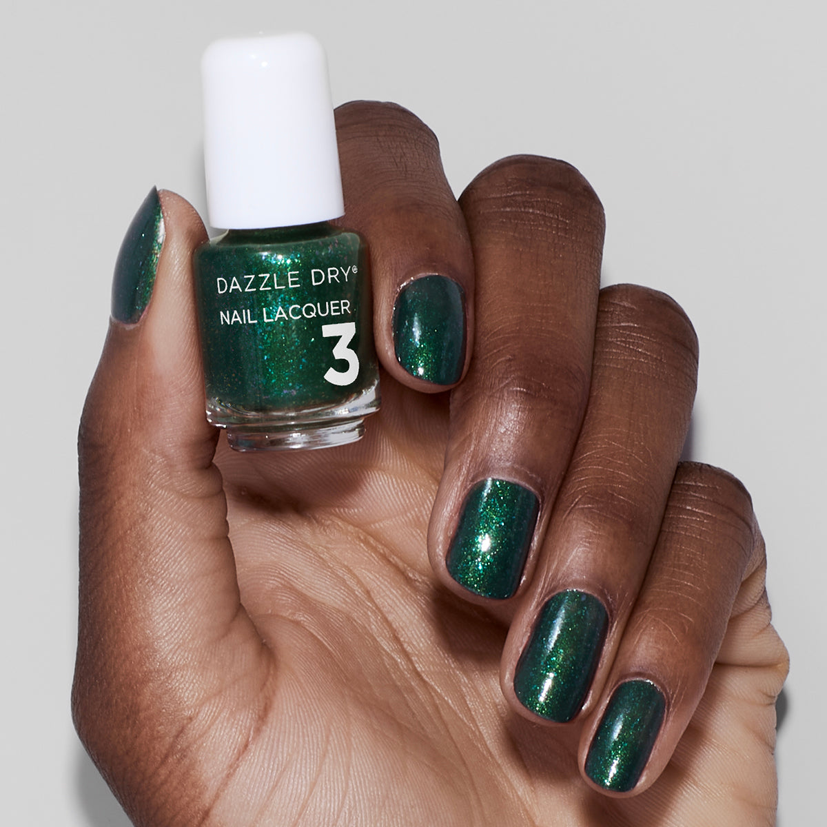 Hand with Evergreen painted on nails holding mini nail lacquer bottle