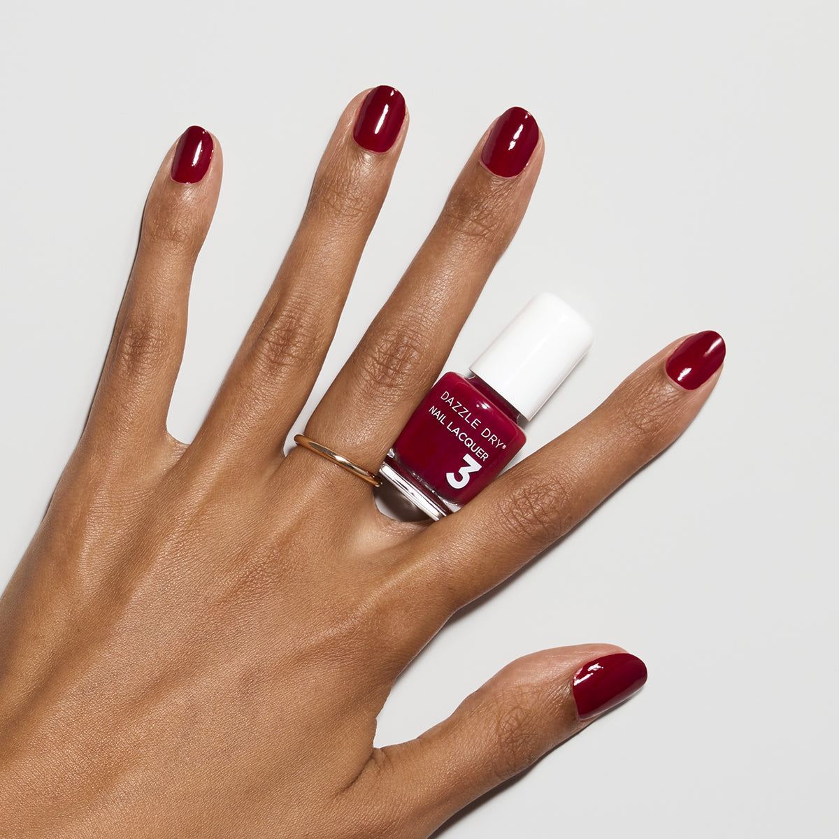 Hand with Fast Track Cherry painted on nails holding mini lacquer bottle