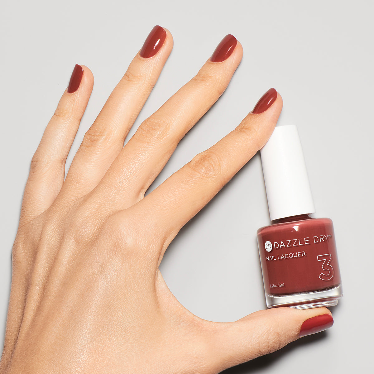 Hand with Cinnamon Spice painted on nails holding nail lacquer bottle