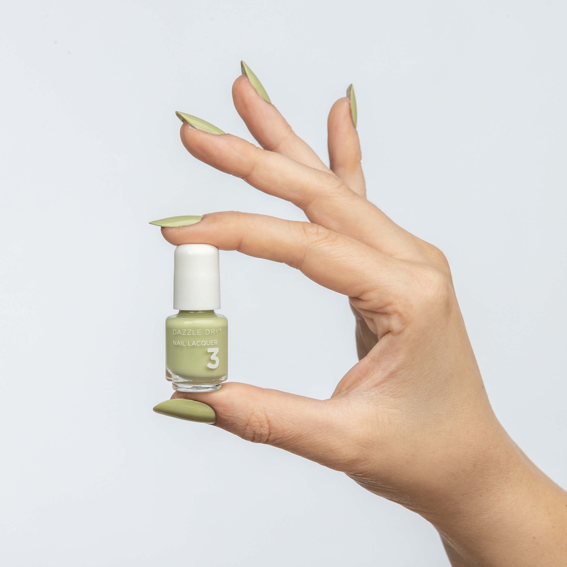 Hand with Pistachio painted on nails holding mini lacquer bottle